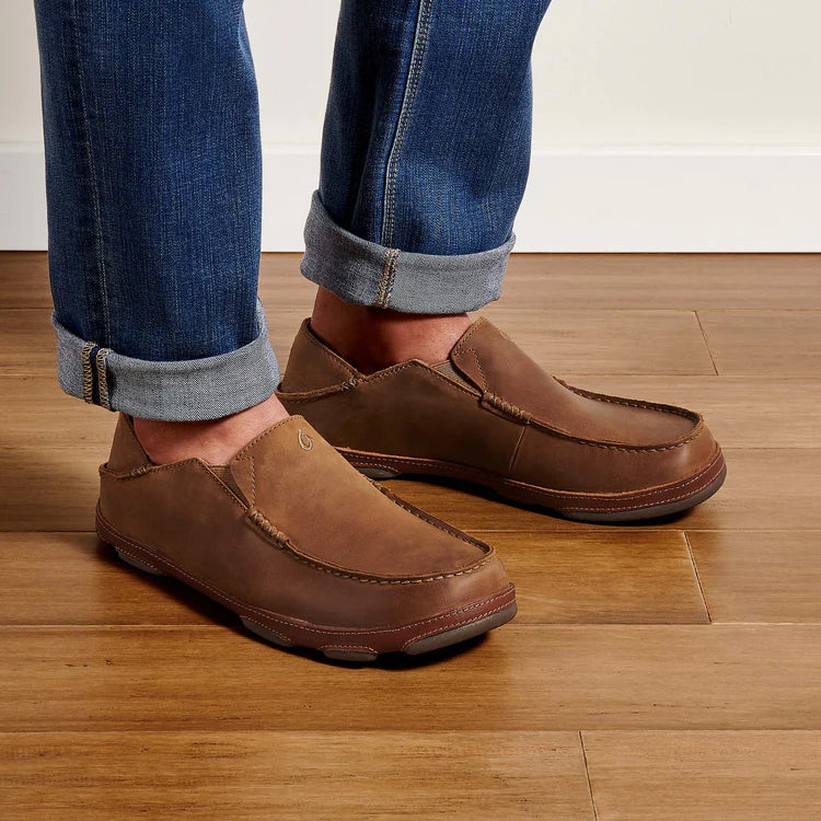 Brown loafers worn with rolled-up jeans on a wooden floor
