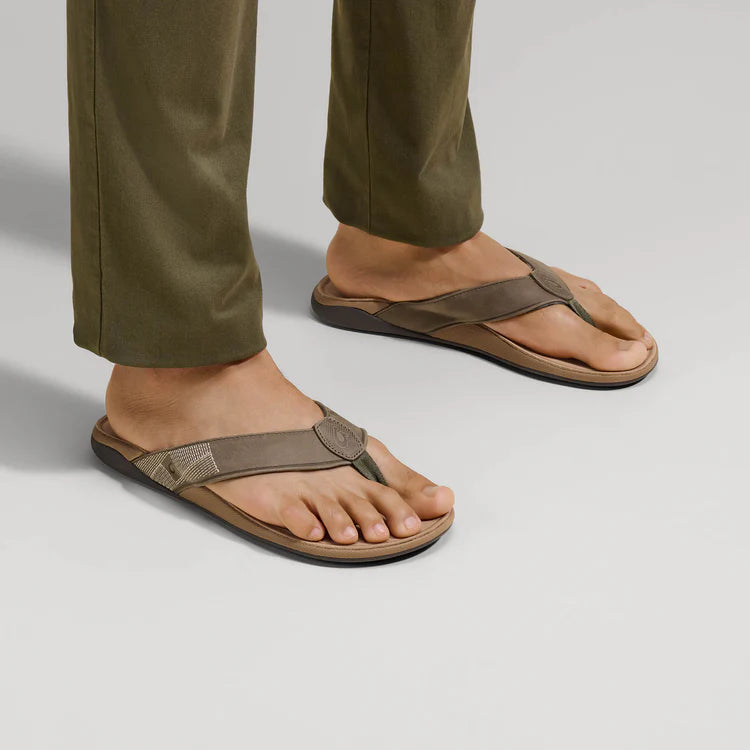 Brown sandals worn with green pants on a light gray background