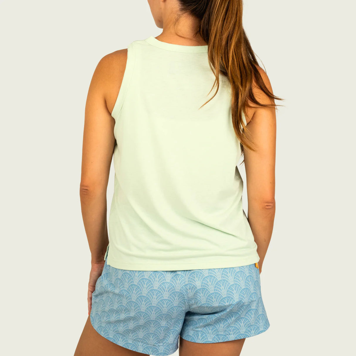 Person wearing a light green sleeveless top and blue patterned shorts on a plain background