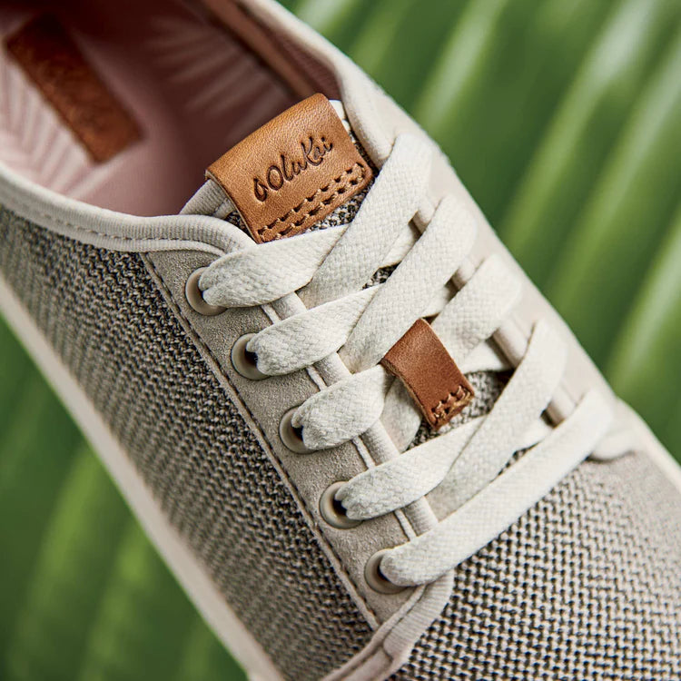 Close-up of a gray sneaker with white laces and brown leather accents on a blurred green background.