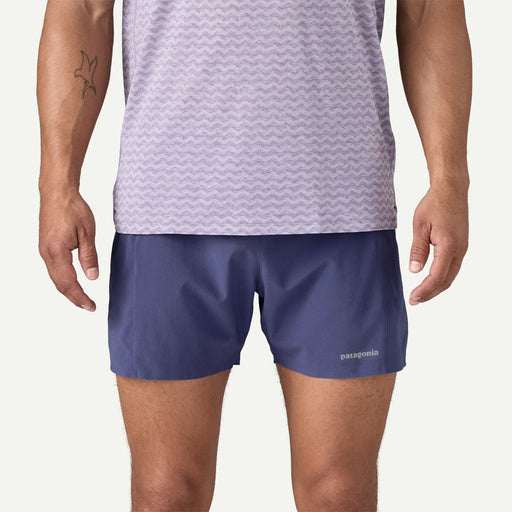 Person wearing a patterned shirt and blue shorts on a plain background