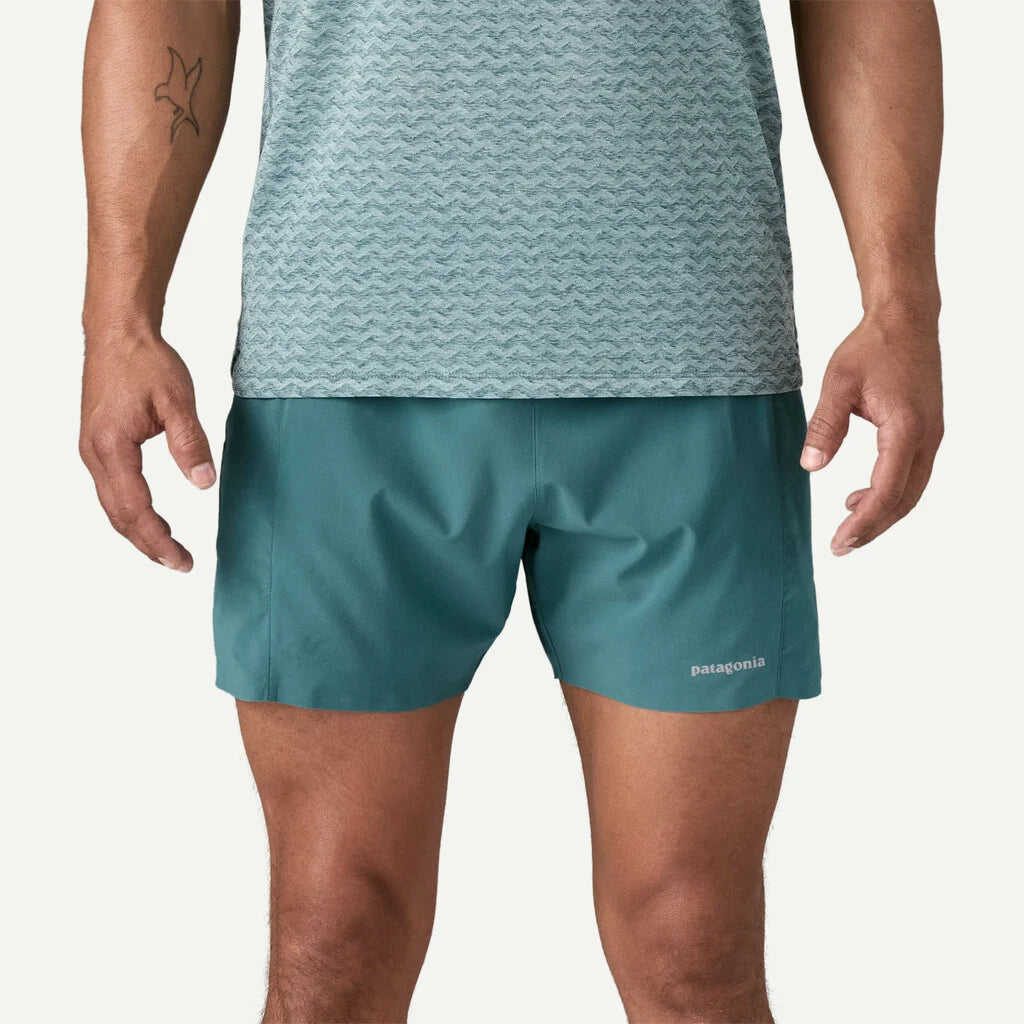 Person wearing teal shorts and a patterned shirt on a white background