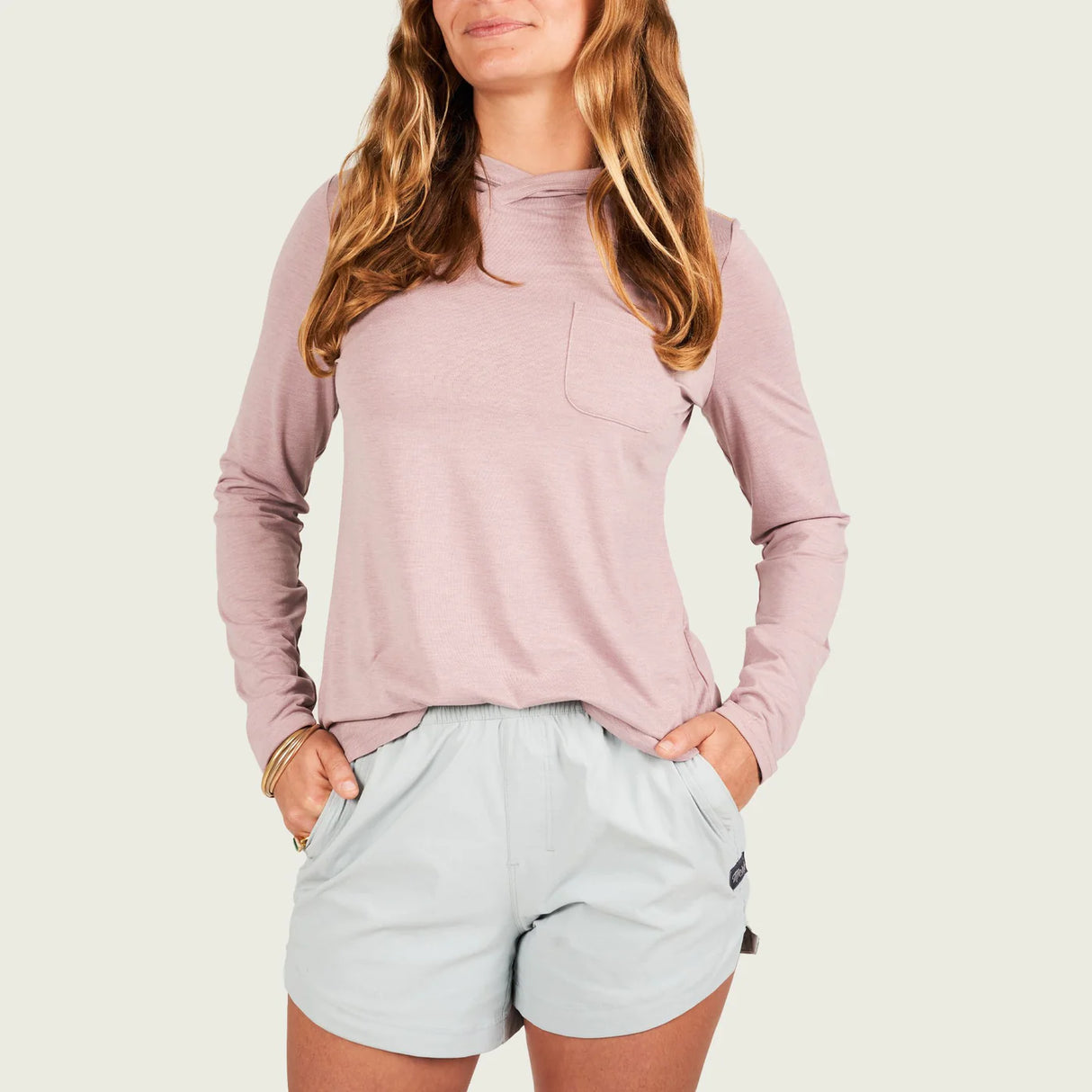 Woman wearing a light pink long-sleeve top and light gray shorts on a white background