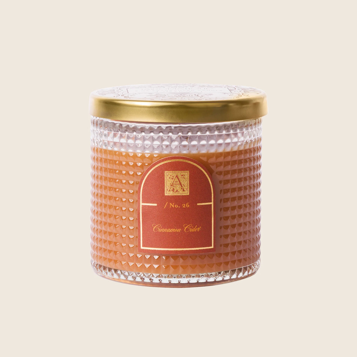 Candle with textured glass jar and gold lid on a beige background