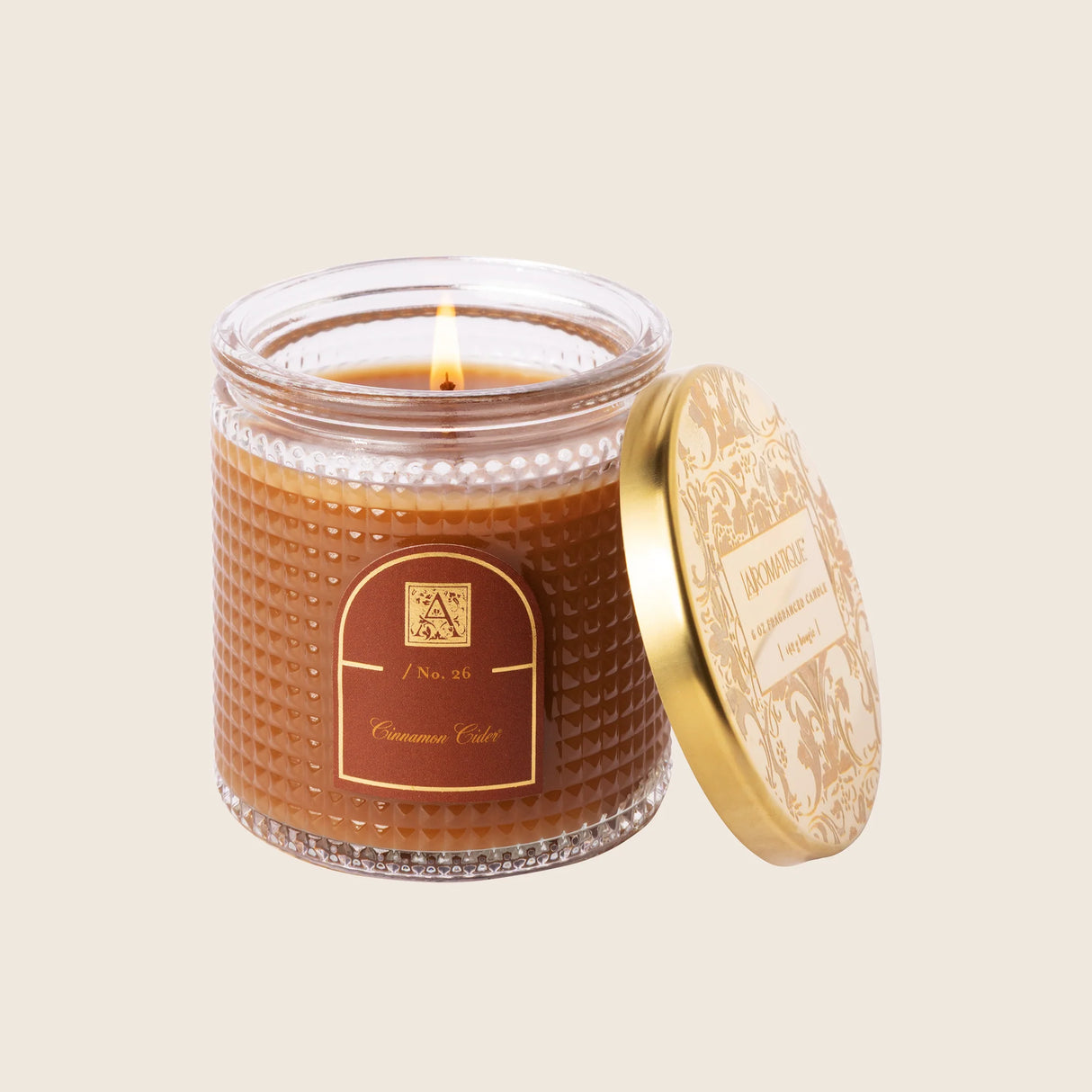 Candle in a textured jar with a gold lid on a beige background