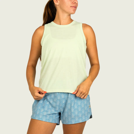 Woman wearing a light green sleeveless top and blue patterned shorts on a white background