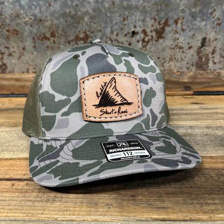 Camouflage trucker hat with leather patch on a wooden surface