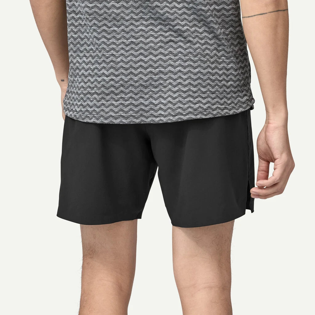 Person wearing black shorts and a gray patterned shirt on a plain background