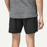 Person wearing black shorts and a gray patterned shirt on a plain background