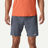 Person wearing gray shorts and an orange shirt with Patagonia branding on a white background