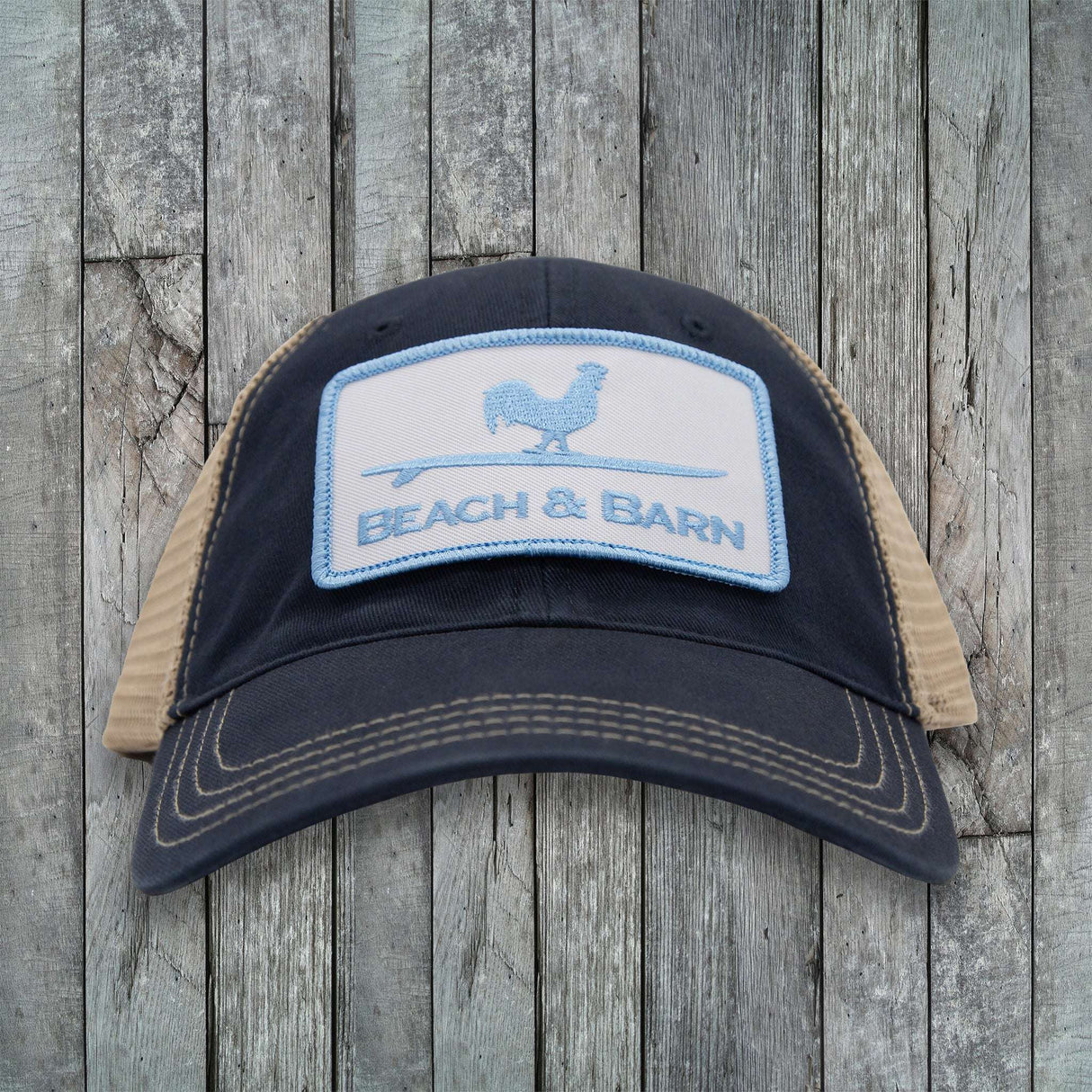 Black and beige cap with 'Beach & Barn' logo on a wooden background